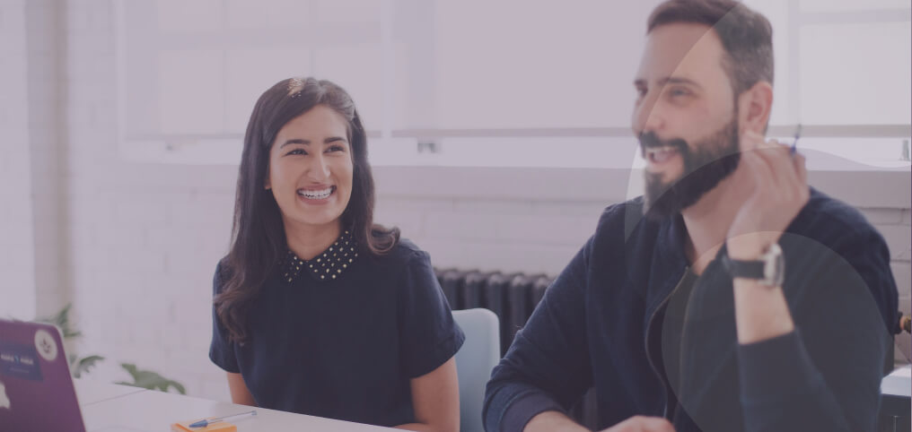 a woman smiling and looking at her coworker while he is talking