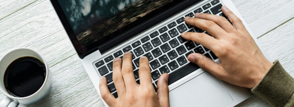 hands typing on laptop, cup of coffee next to laptop