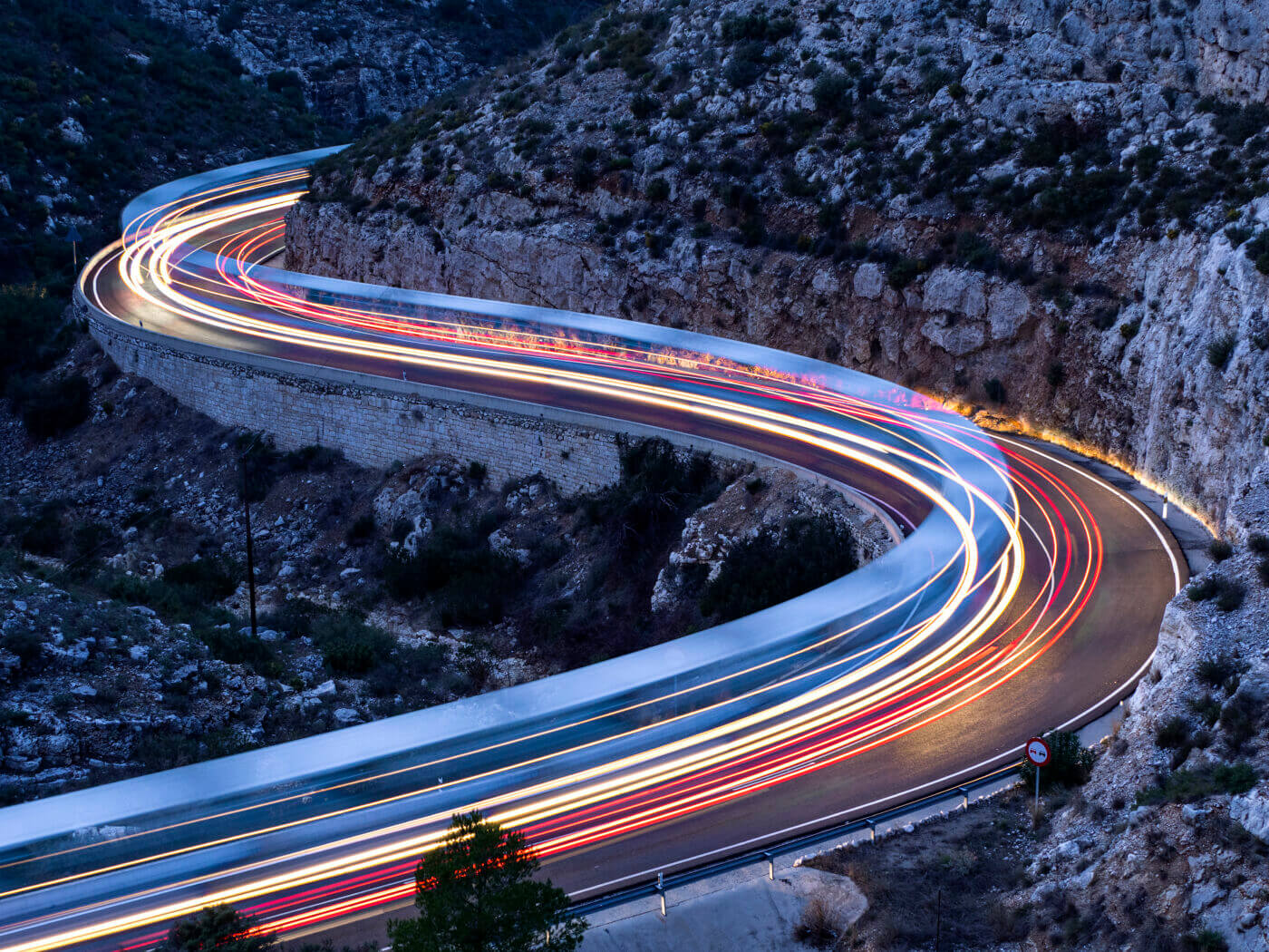 Lights and trails of vehicles, cars and trucks, circulating along a road of mountain between ravines with circular curves closed in the nightfall.