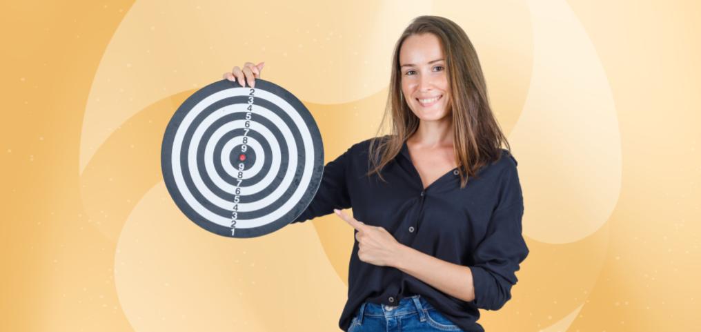 Eine lächelnde Frau hält eine Zielscheibe hoch und zeigt mit dem Finger darauf.